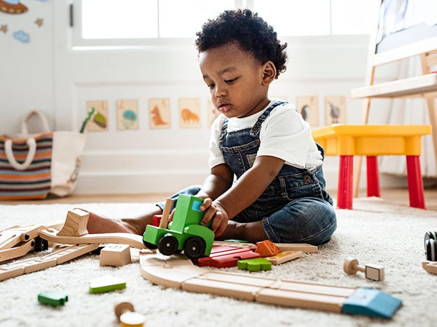 Child playing on the floor looking at a wood train
