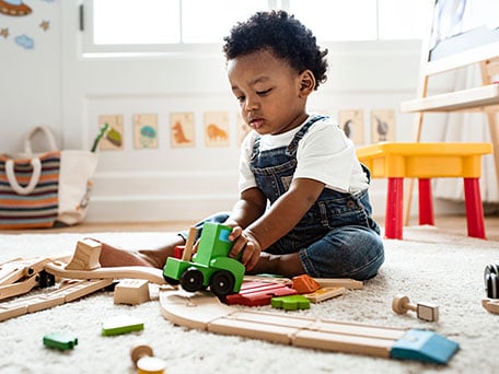 Child playing on the floor looking at a wood train